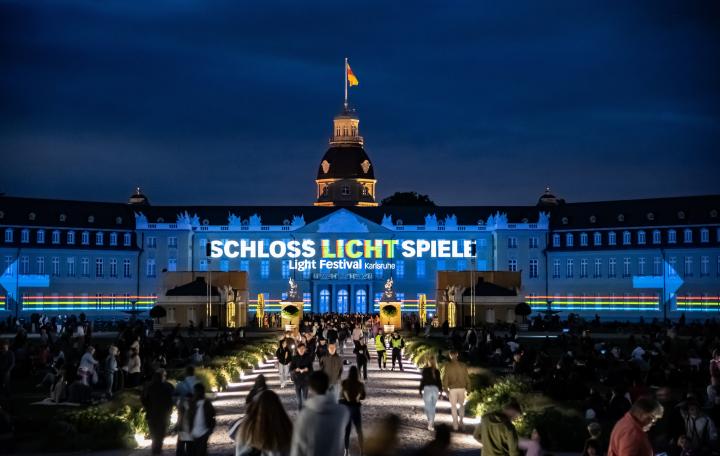 Photo of a colorful projection mapping at night on the baroque Karlsruhe castle. You can see the text »Schlosslichtspiele«