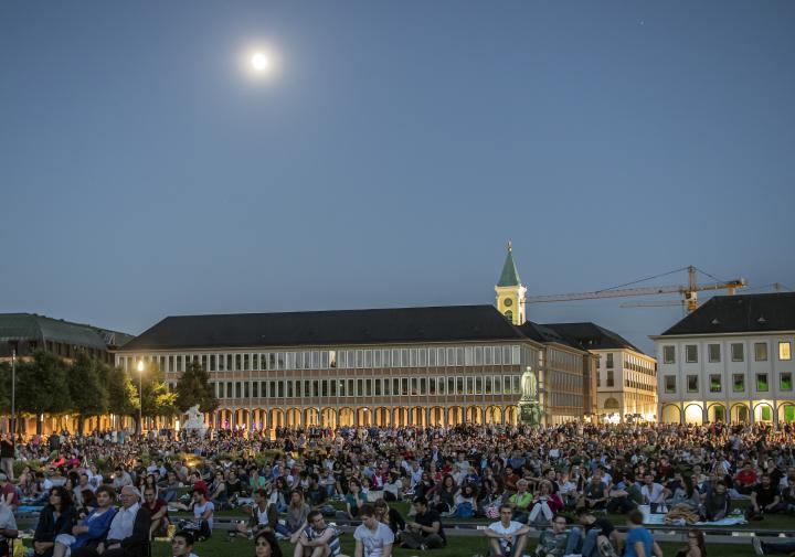 The image shows the forecourt of Karlsruhe Palace, filled with the audience of the Schlosslichtspiele