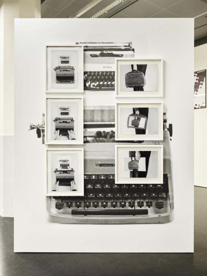 Das Foto zeigt eine schwarz weiße Fotocollage. Der Hintergrund wird von einer alten Schreibmaschine gebildet und auf dieser hängen 6 gerahmte schwarz/weiß Bilder die abwechseln eine Aktentasche und eine Schreibmaschine zeigen.