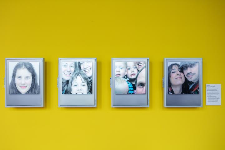 gelbe Wand mit vier Monitoren, die Gesichter zeigen