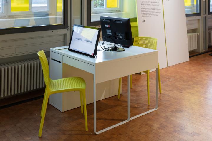 Ein Tisch mit zwei gelben Stühlen und zwei Bildschirmen