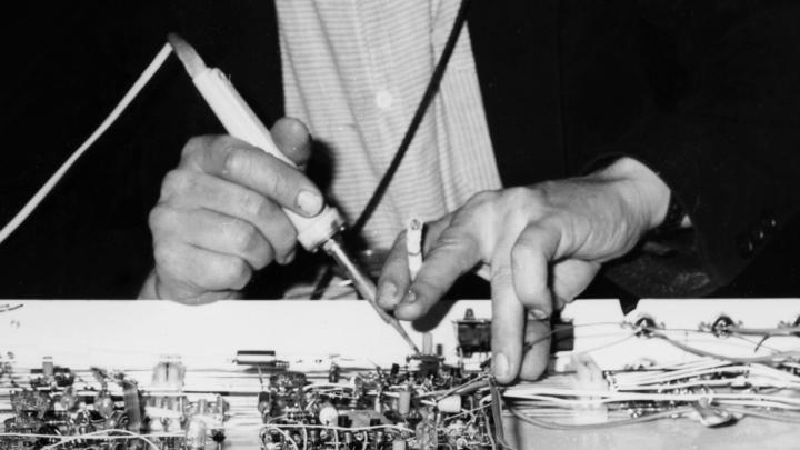 Two male hands can be seen. In one of them a cigarette. The man is fiddling around with electronic works.