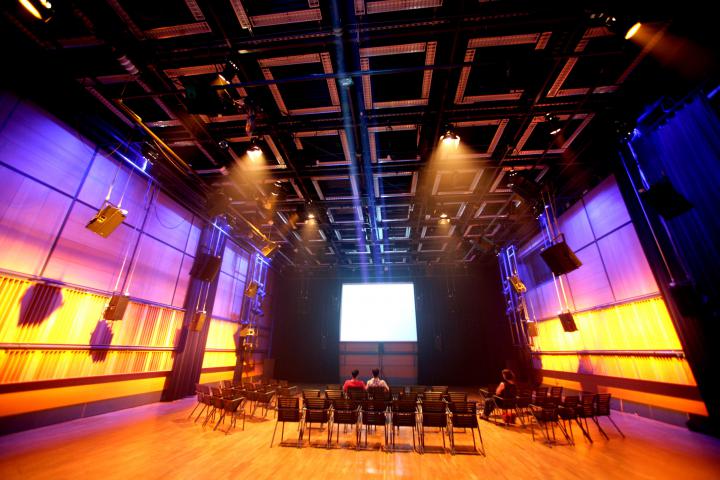 A white screen in the background. Previously, a number of chairs. The side walls are bathed in a purple and yellow light.
