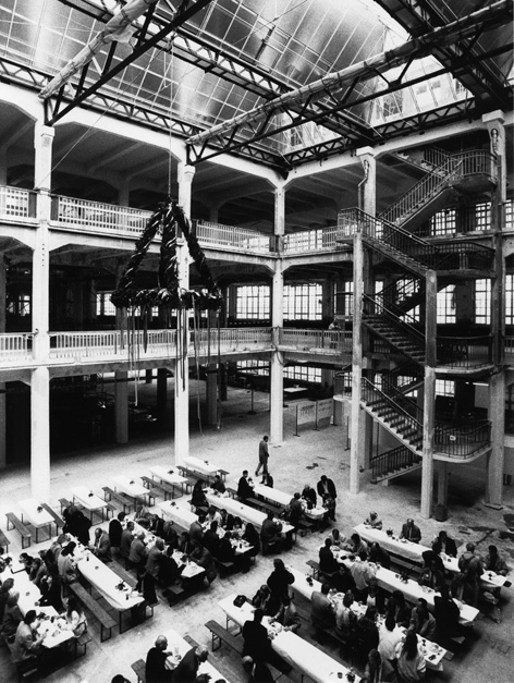 S/W Fotografie der Feierlichkeiten zum Richtfest im Hallenbau. Besucher sitzen an Bierbänken. Über ihnen der Richtkranz.