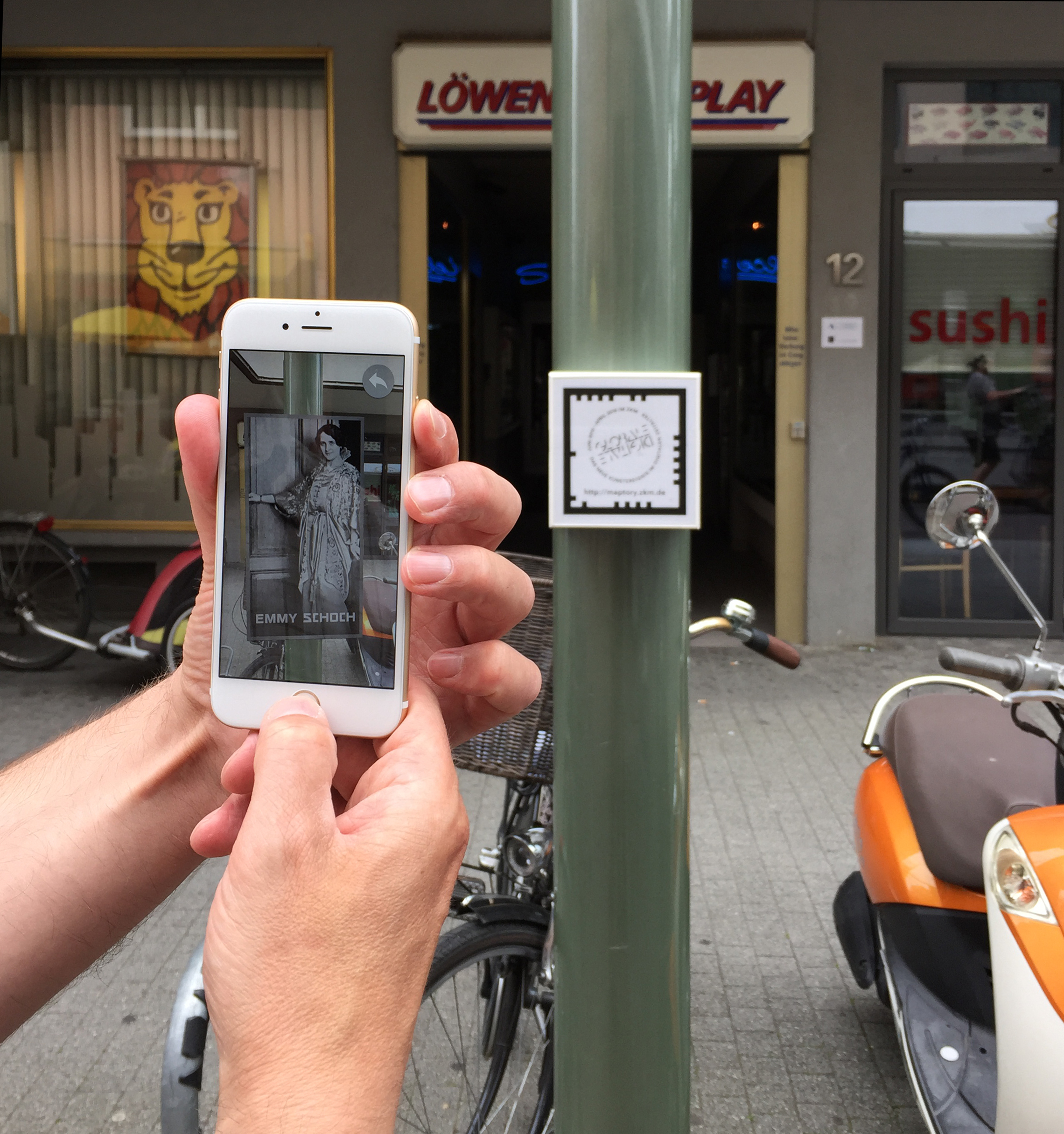 Ein Smarthphone wird hochgehalten, um den Augmented-Reality-Marker auf einer Säule zu erfassen.