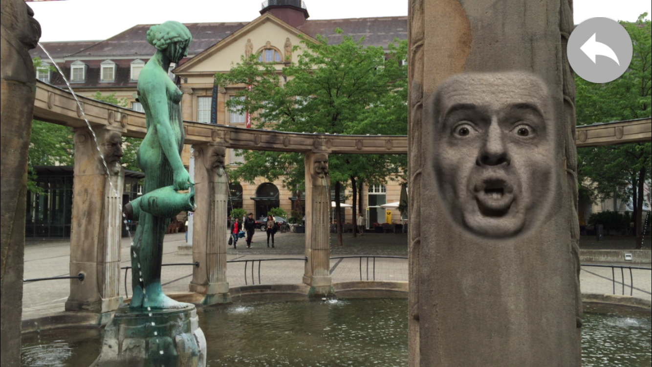 Blick auf den Stephanienbrunnen am Stephansplatz: auf der Säule ist die Projektion eines sprechenden, männlichen Gesichts zu sehen.