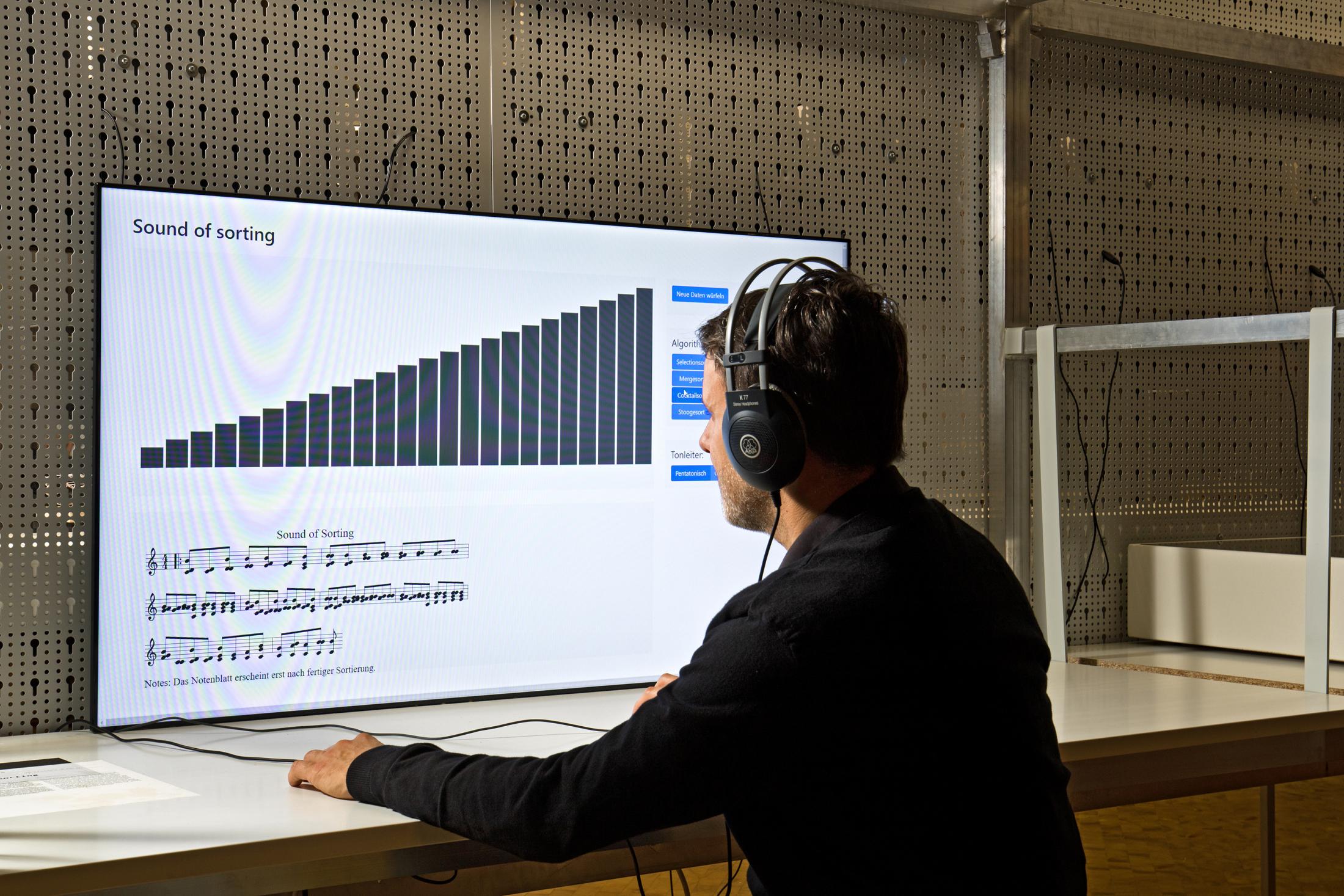 The picture shows a sitting man with headphones in front of a large screen with a sound simulation program