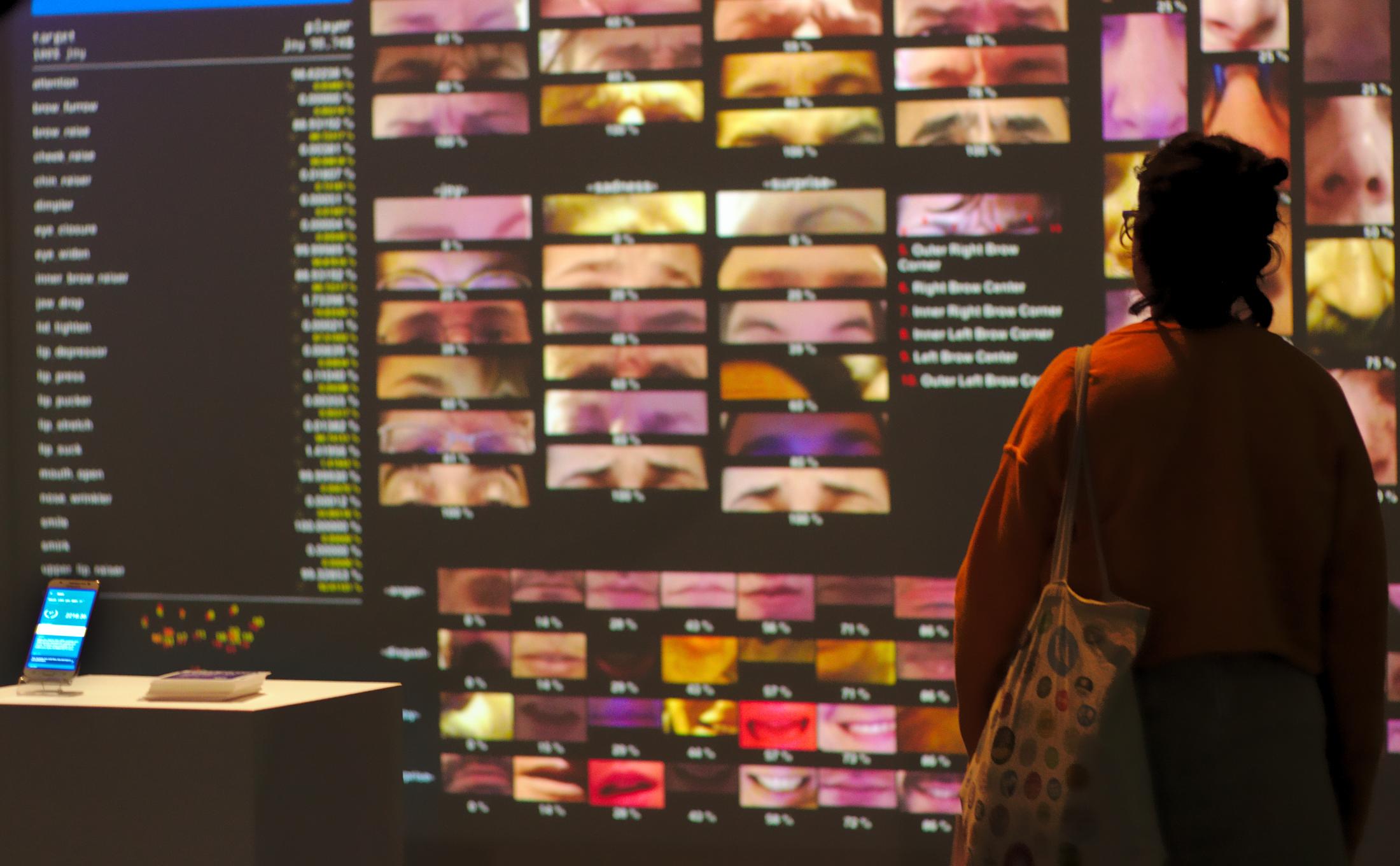 A person stands in front of a screen showing face recognition patterns 