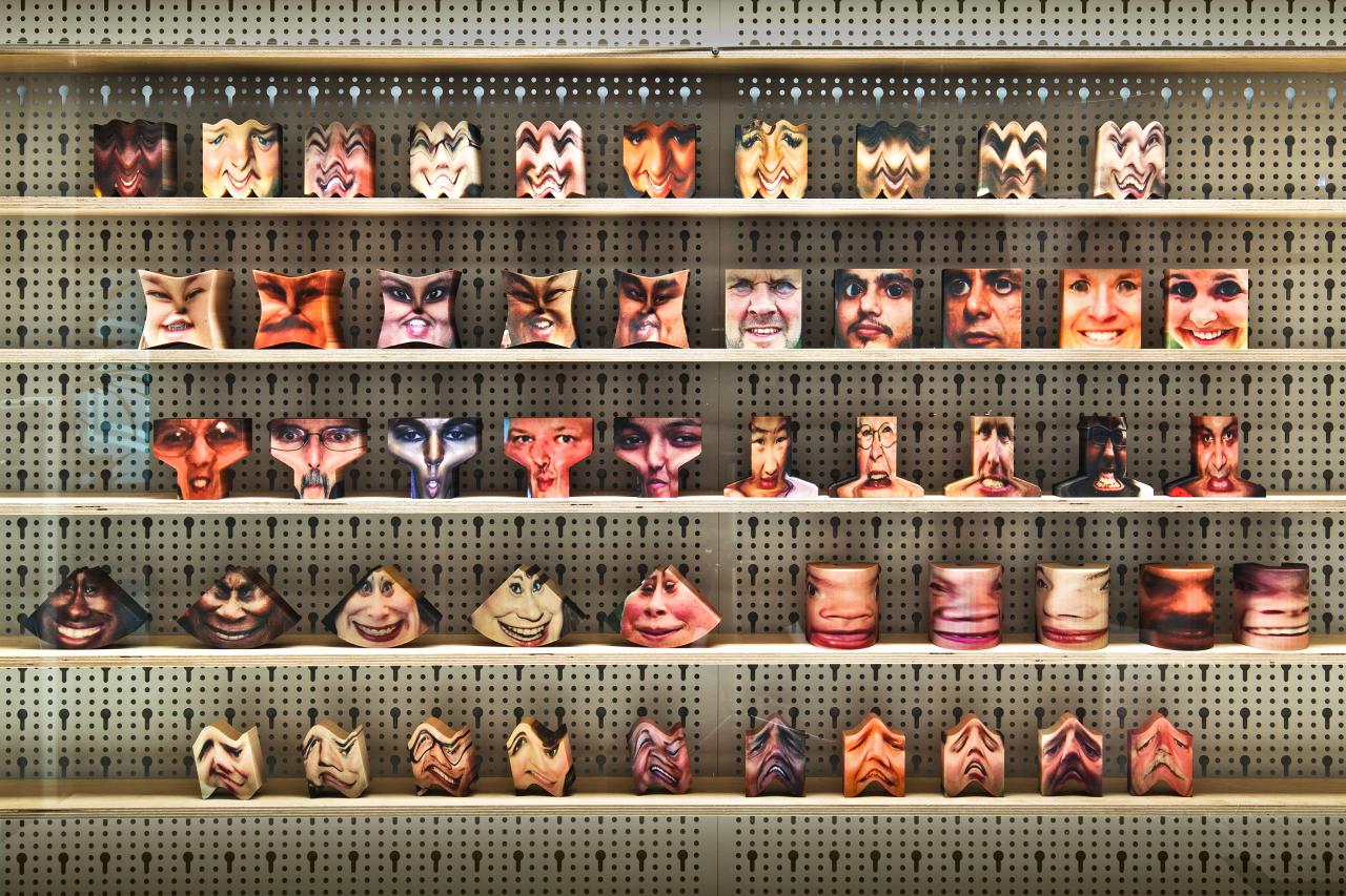Installationsansicht verschiedener Objekte mit aufgezogenen Gesichtern in einem Regal