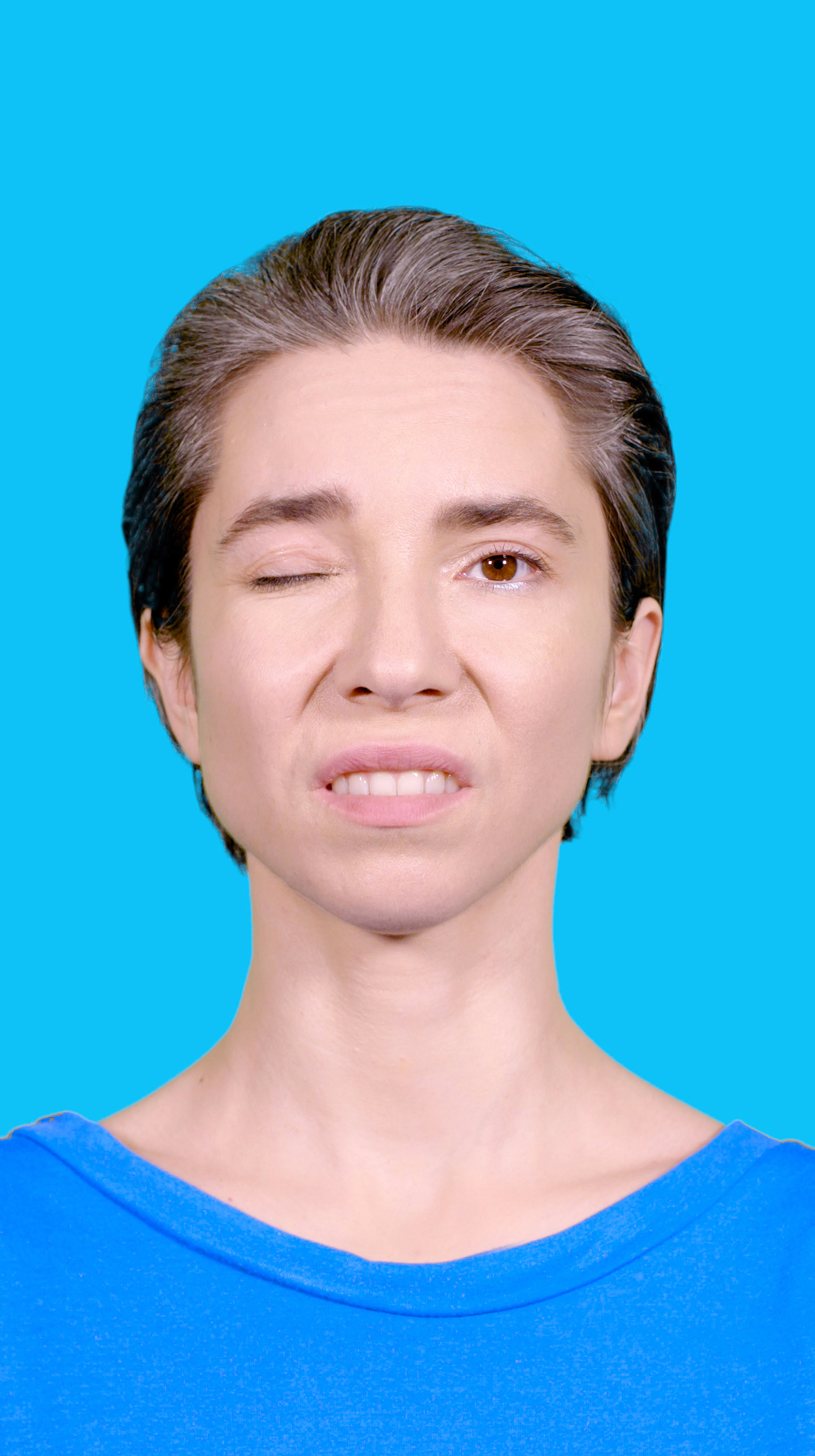 Der Screenshot zeigt eine Frau, die frontal mit einem geschlossenen und einem offenen Auge in die Kamera schaut.