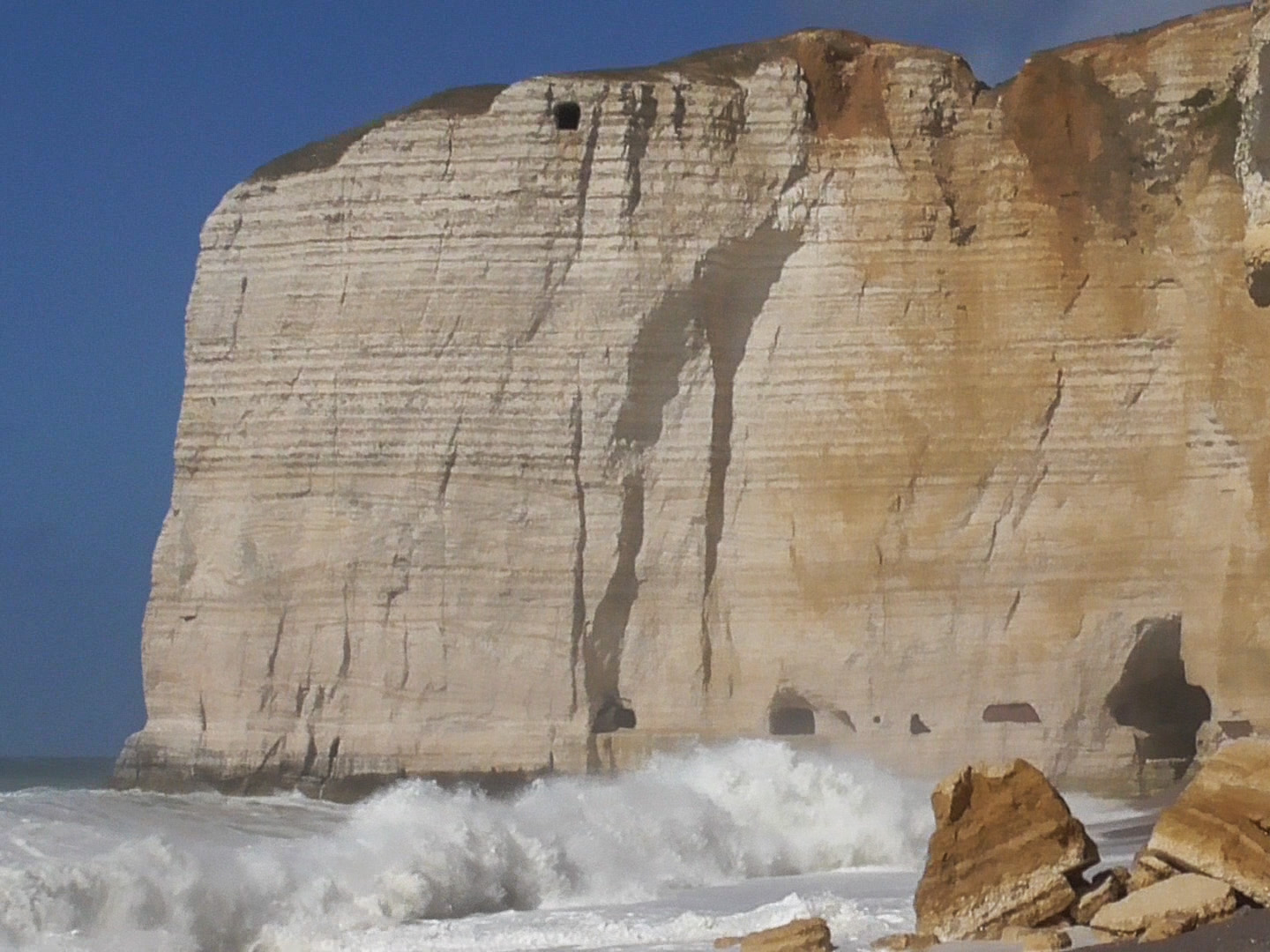 An enormous rock fills almost the whole picture. At its foot the waves are crashing hard, at its top a cloudless summer sky is stretching.