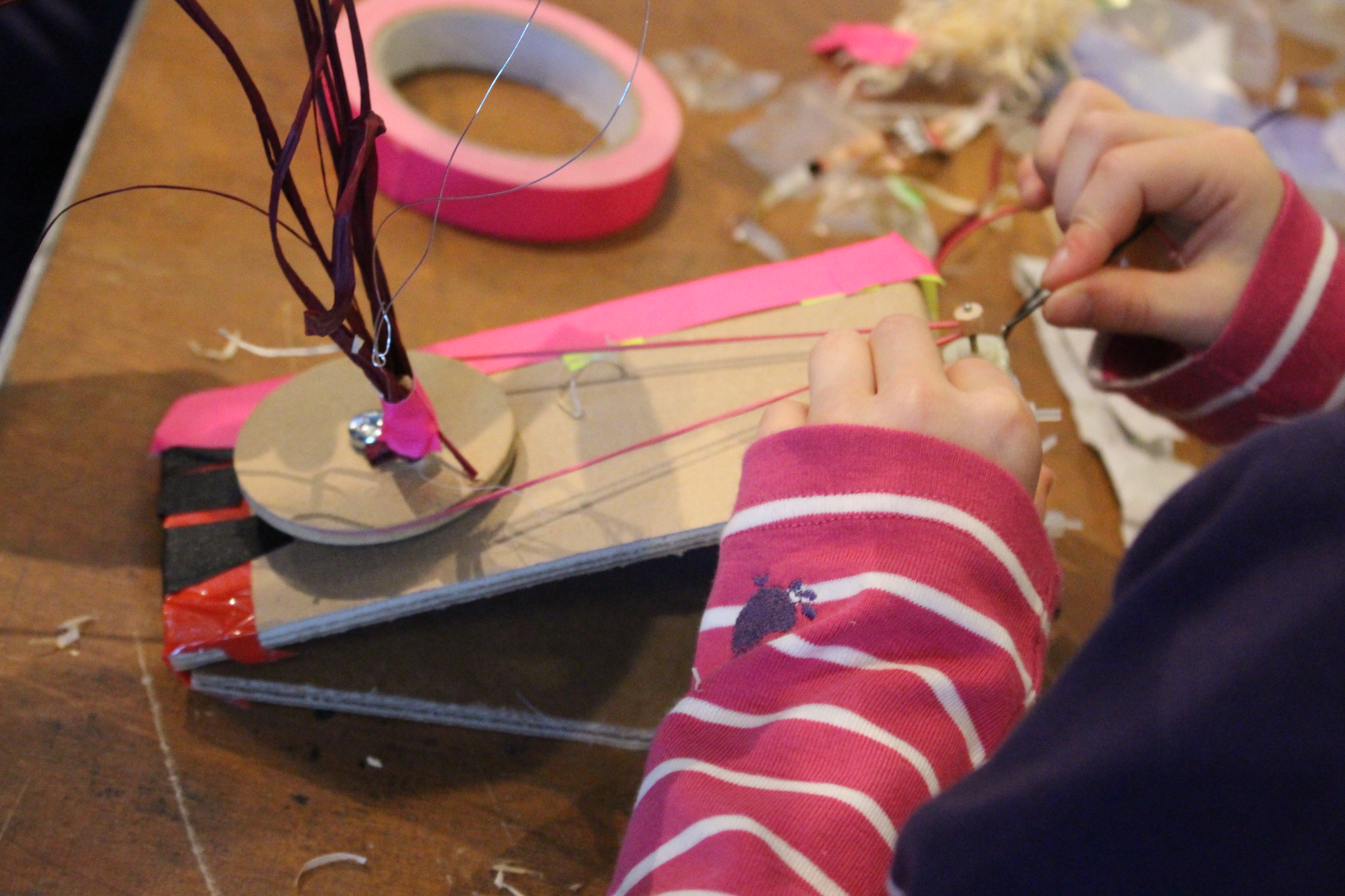 A kid works on a little automated construction, that it has equipped with a wheel, that is going to be rotated by a rubberband and a small motor.