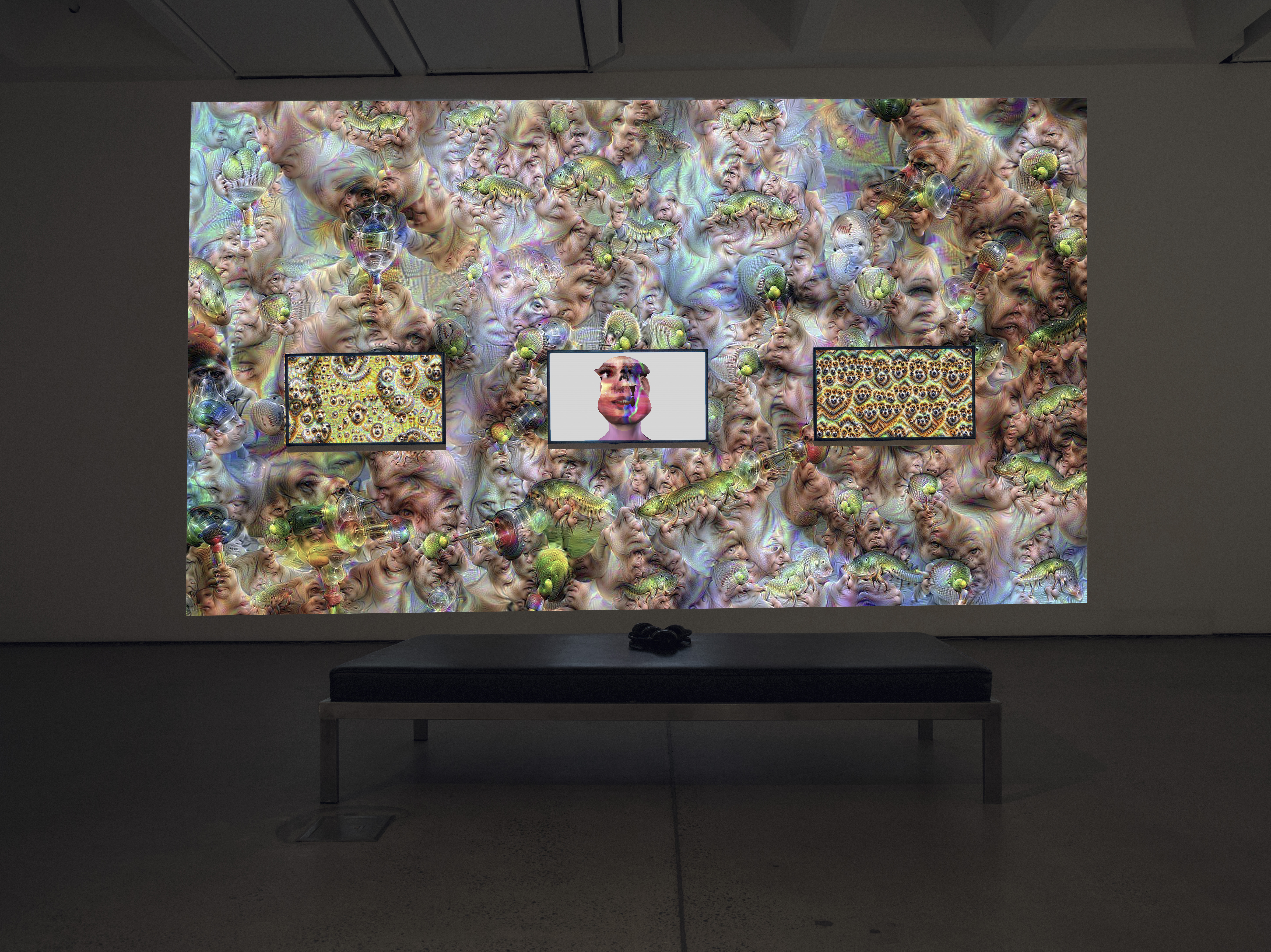 The photo shows an exhibition view of the work »im here to learn so :))))))«. Shown is a large screen in the background and three screens in the foreground. They show psychedelic cosmos and the chatbot Tay.