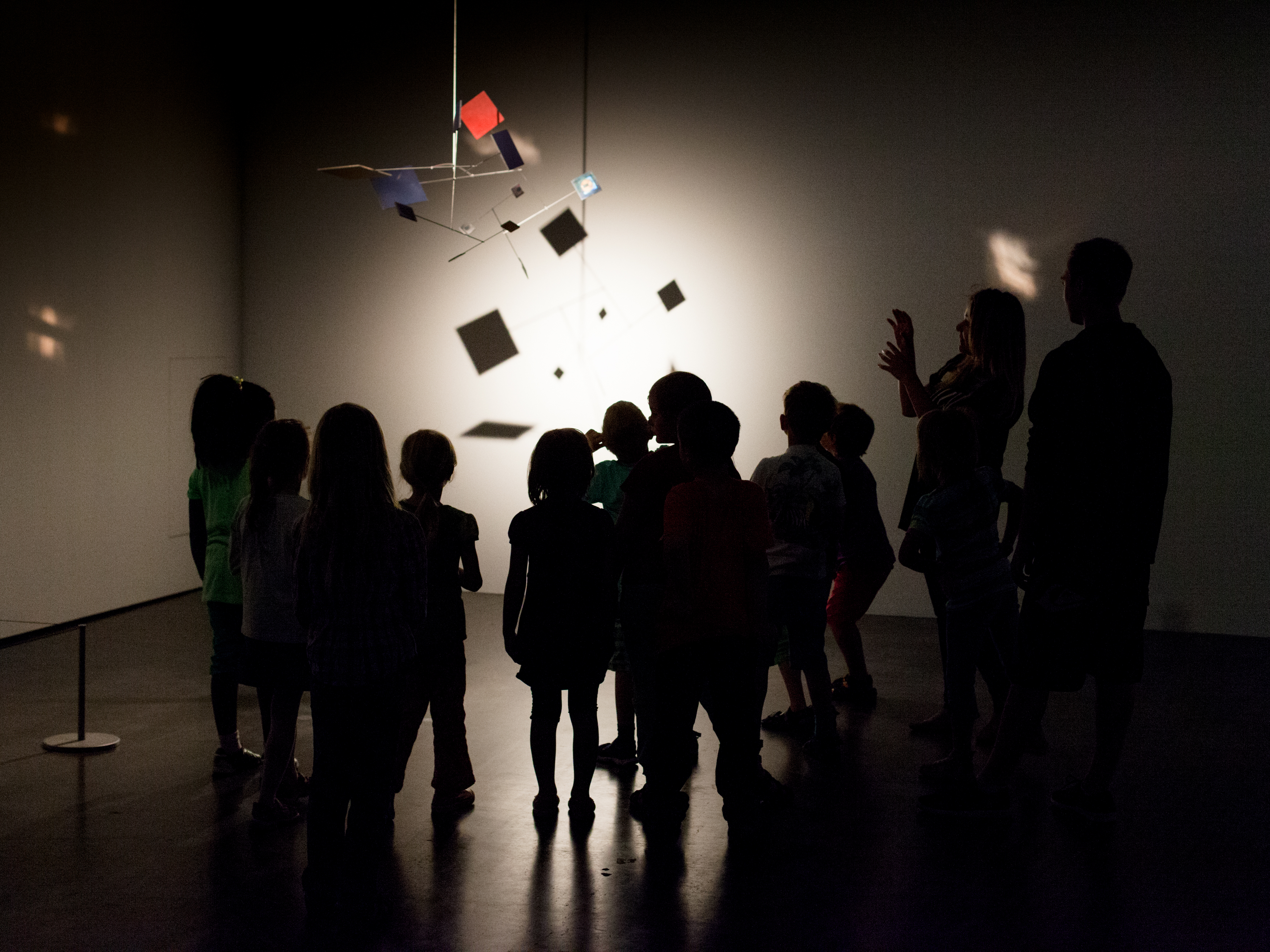 im dunkeln Museum stehende Kinder betrachten ein Mobile, das vom Licht angestrahlt wird