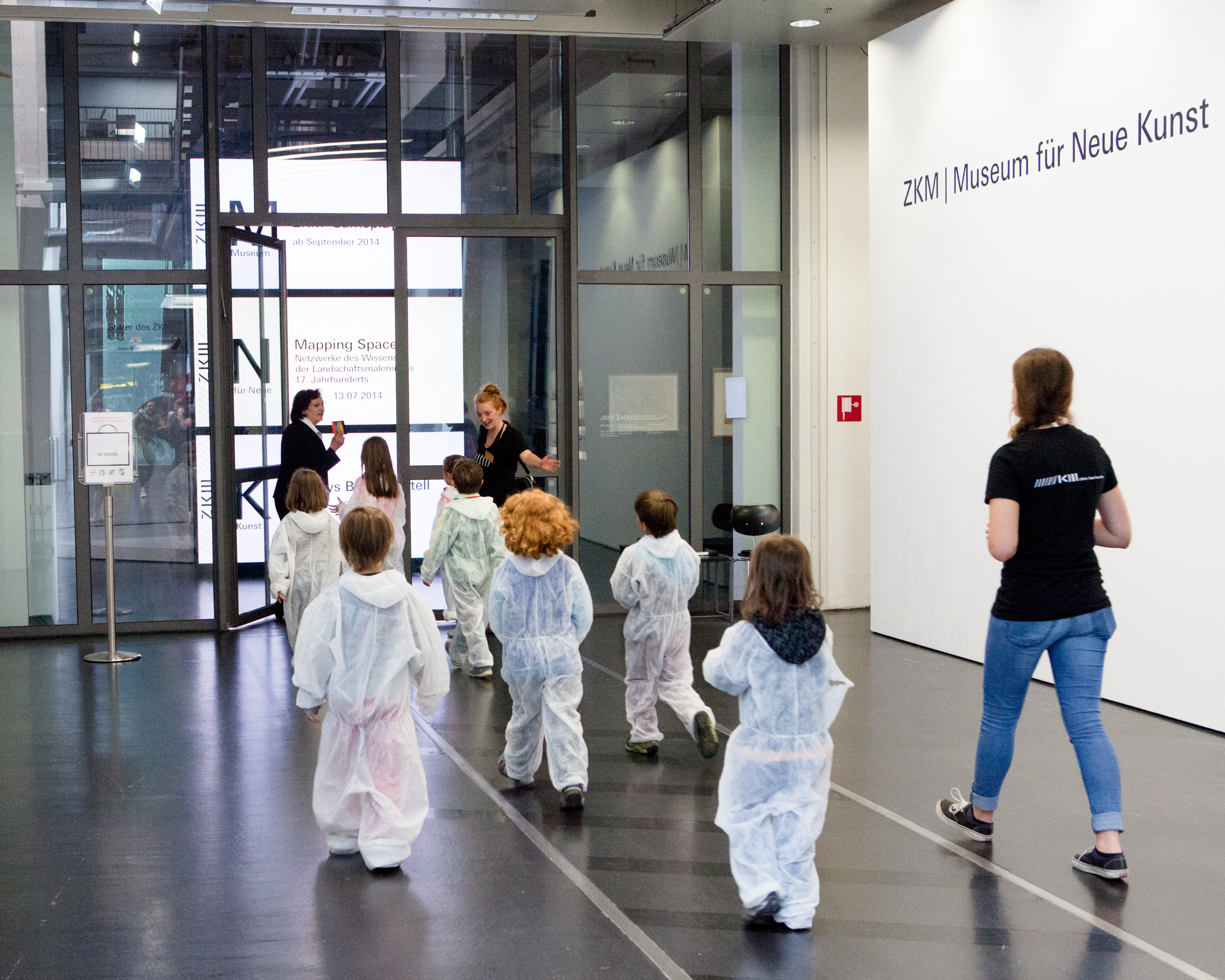 Kinder in weißen Overalls betreten das Museum für Neue Kunst