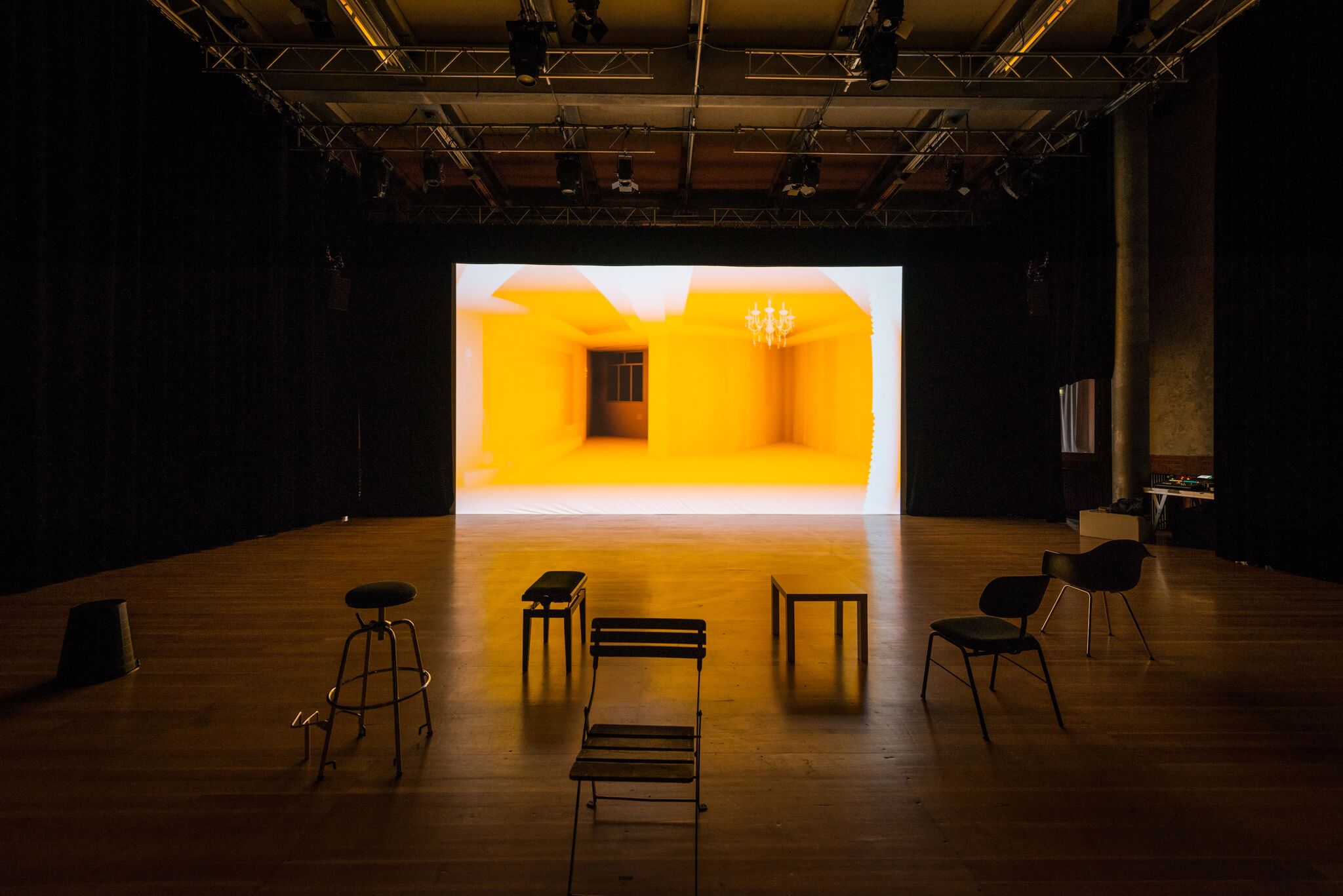 Exhibition view of the work »Homeschool« by Simone C. Niquille / Technoflesh in a darkened room, some seating and a large screen on which a yellow interior is projected