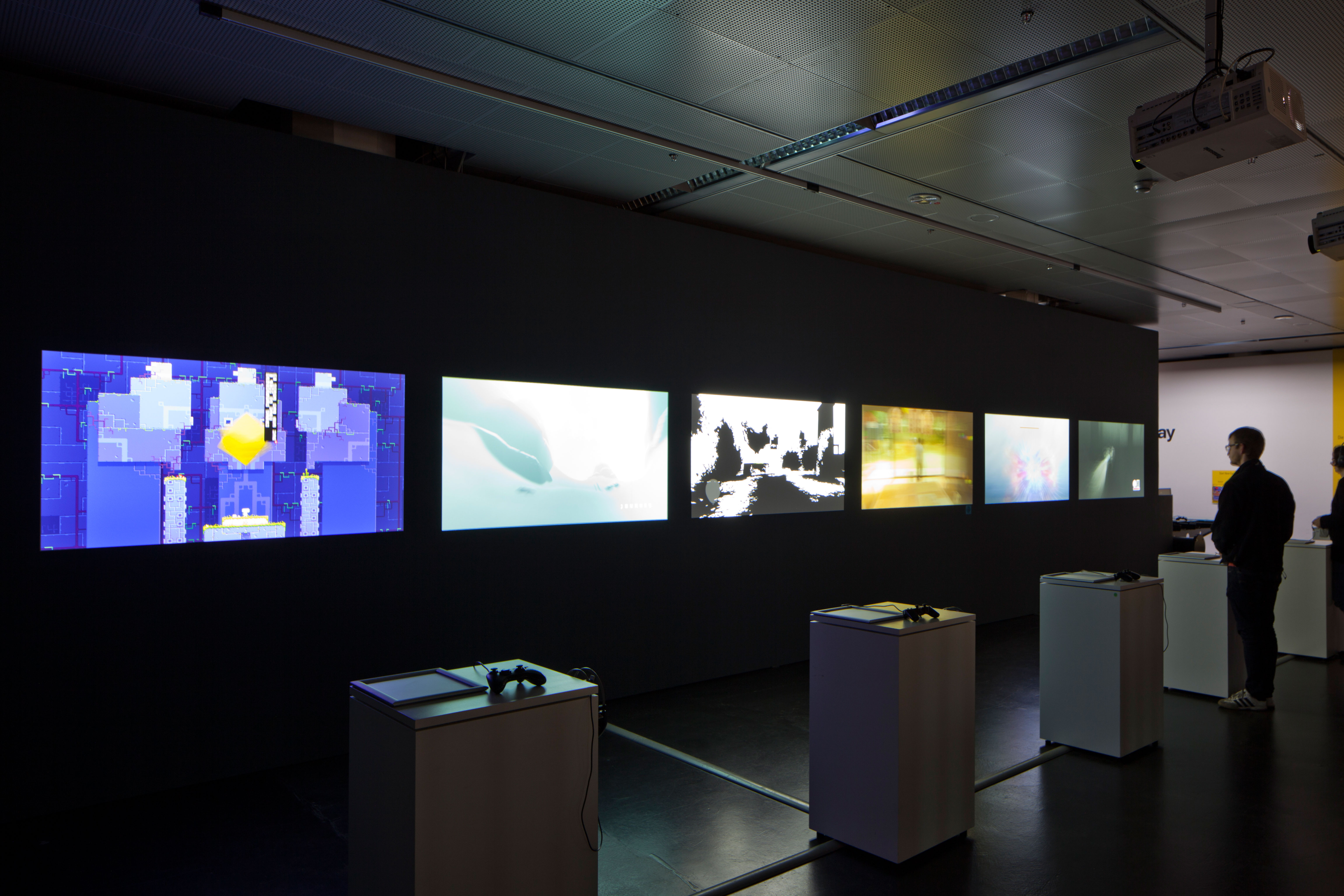 Mehrere Computerspiele auf Leinwand gebeamt. Eine Person an einer Spielkonsole.