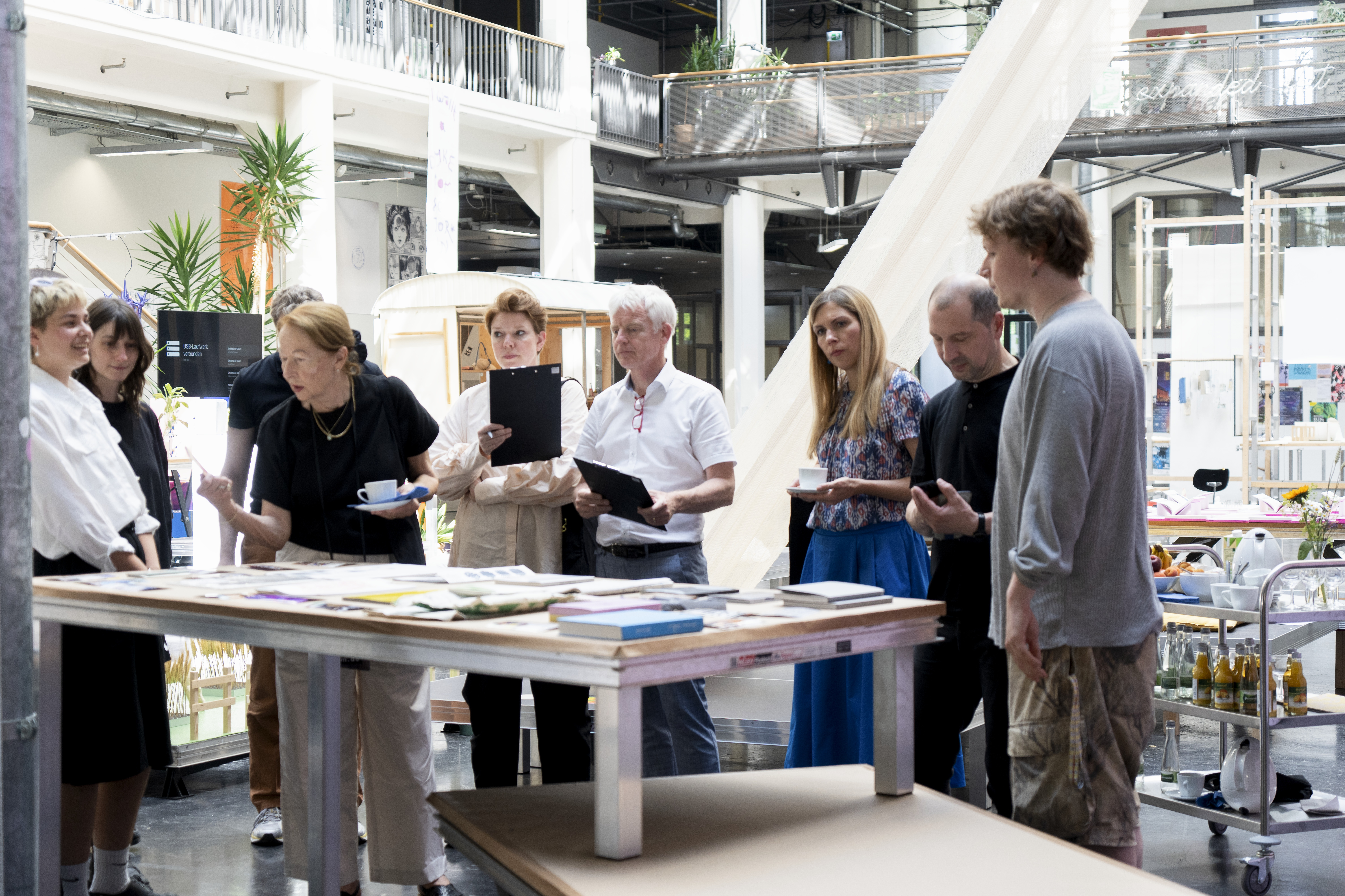 Personen mit Mappen stehen vor einem Tisch mit Büchern und diskutieren.
