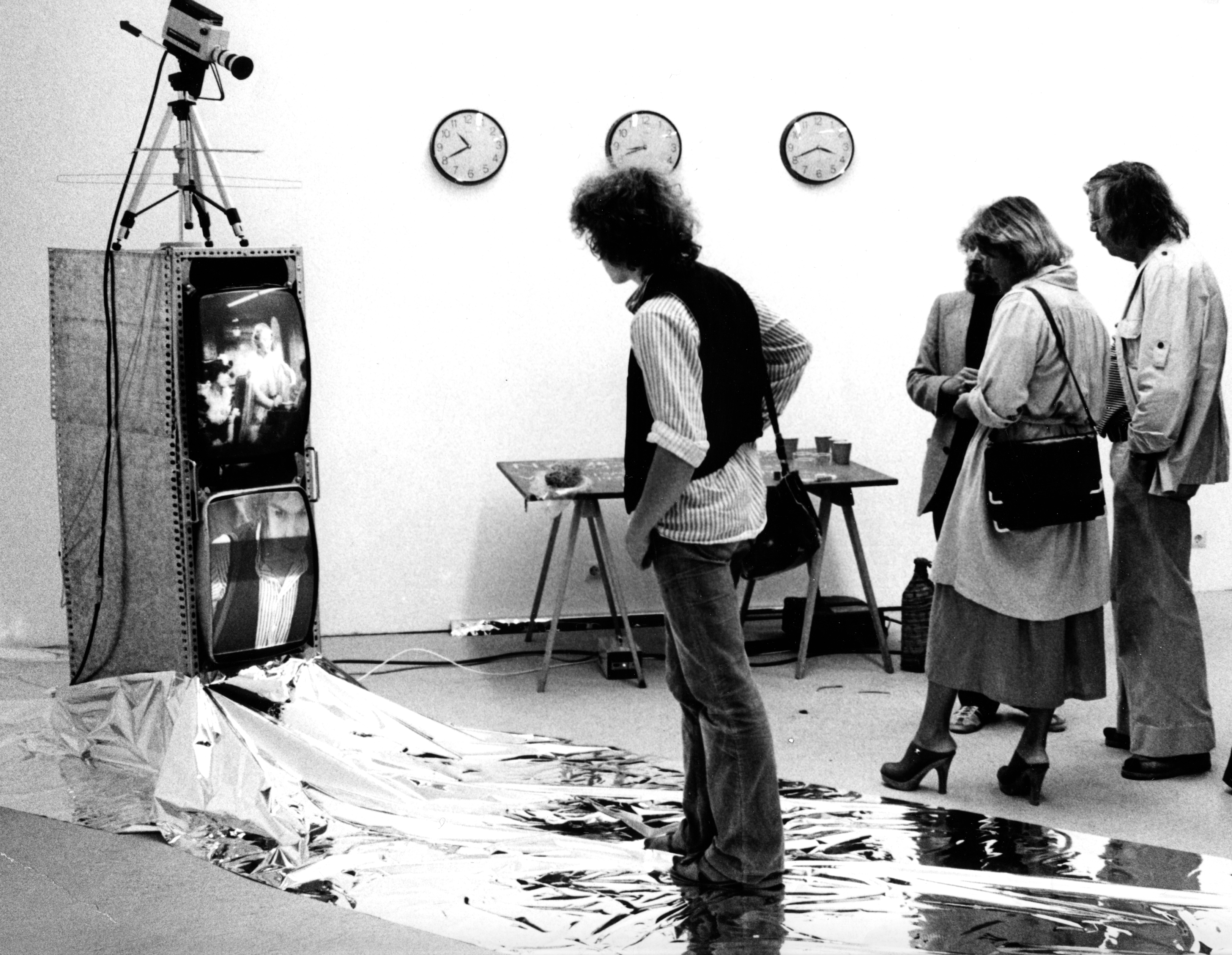 Schwarz-Weiß-Aufnahme von vier Personen, die auf eine Videoinstallation blicken. 