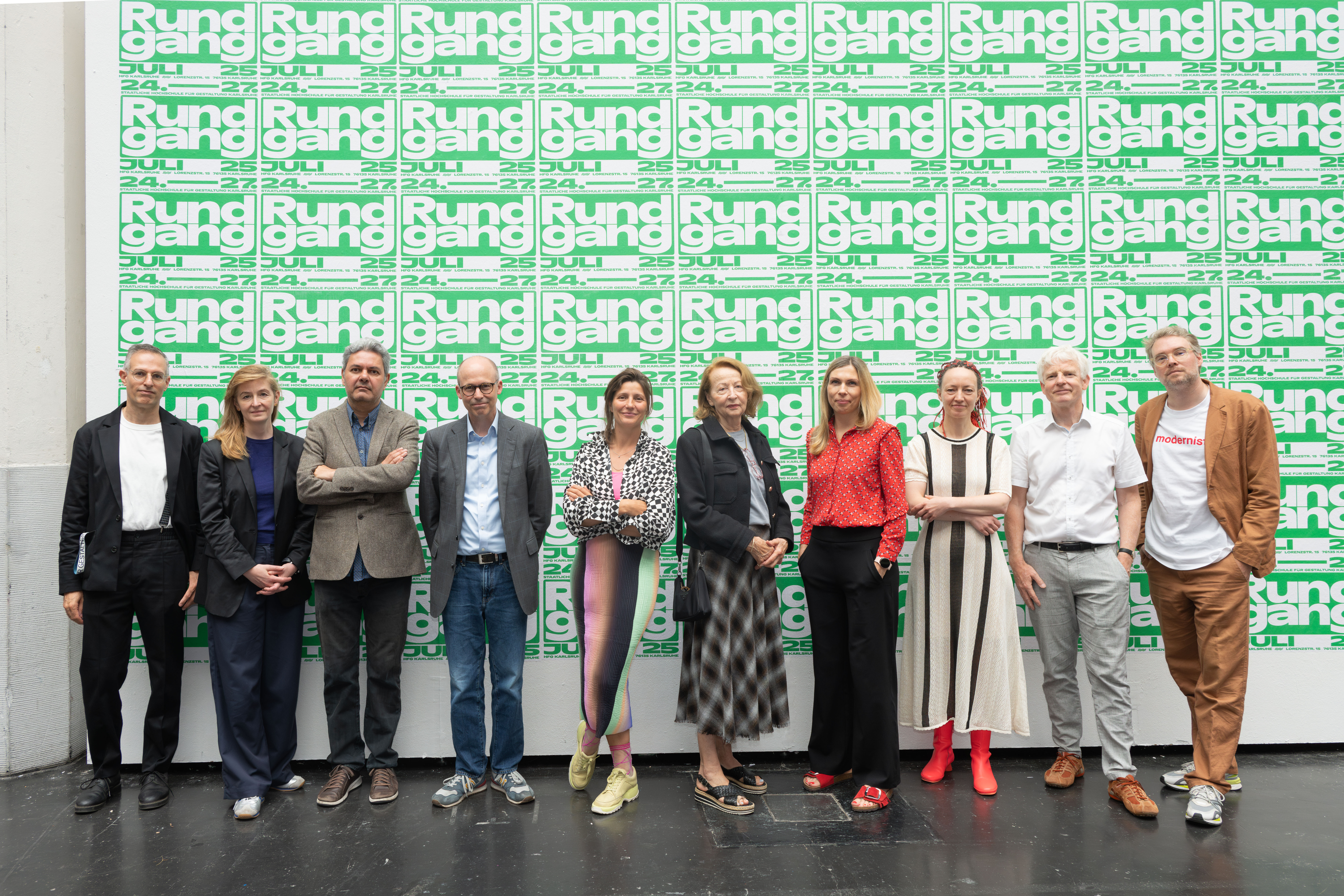Zu sehen sind zehn Personen vor einer großen Plakatwand. 