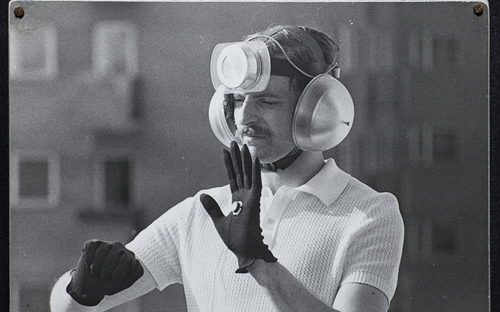 The black and white photo shows a man with a technical installation on his head, his ears covered with sound barriers.