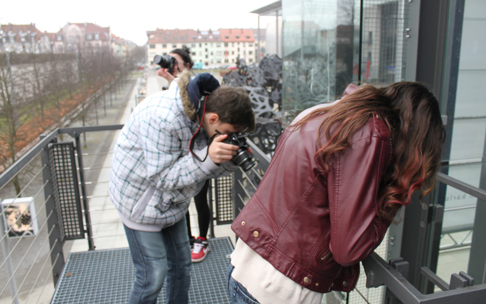 Three youngsters are taking photos on the stairs in front of the ZKM in different directions.