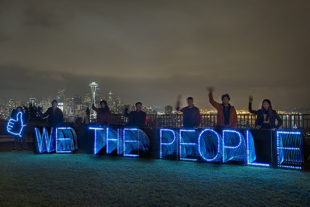 »We the people« lettering in blue light in front of a city silhouette