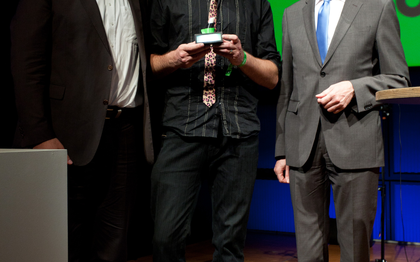 Three man standing next to each other while the one in the middle is holding an award