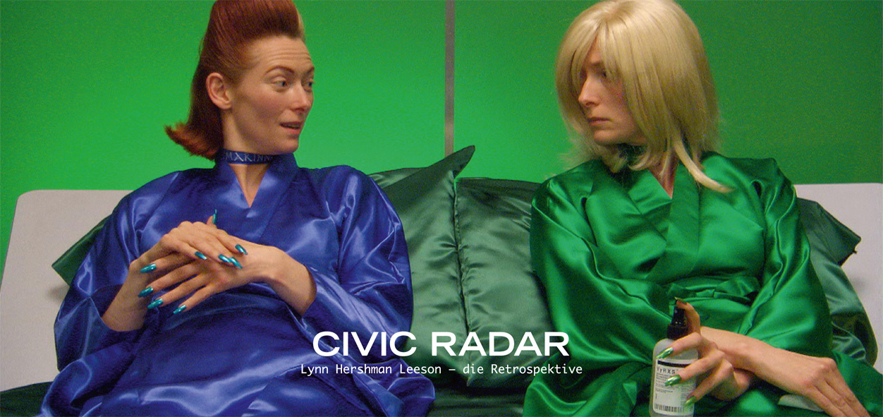 A woman in two different appearance. On the left side in the blue silk coat and brown hair, on the right side in the green silk coat and blond hair. Both sit together and look at each other.