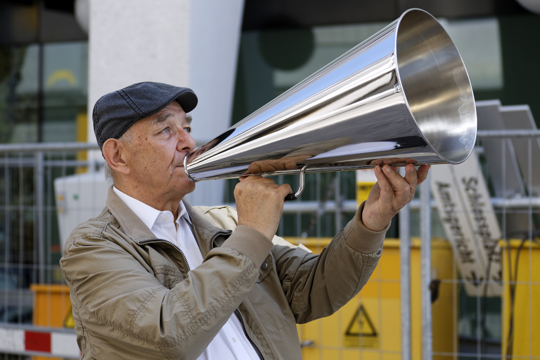 A man stands on the street with a silver megaphone