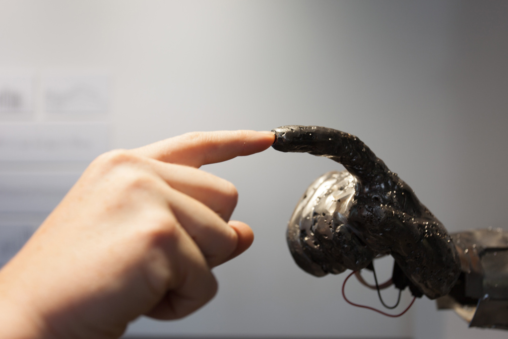 A human finger touches a finger of a sculpture