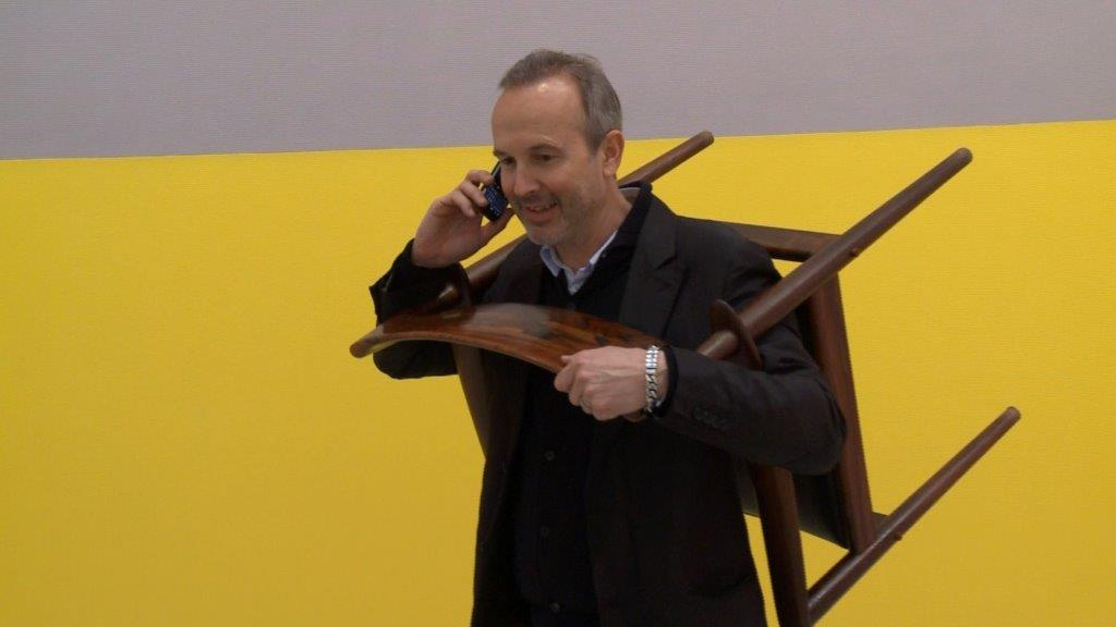 A man at the telephone, wearing a chair around his neck