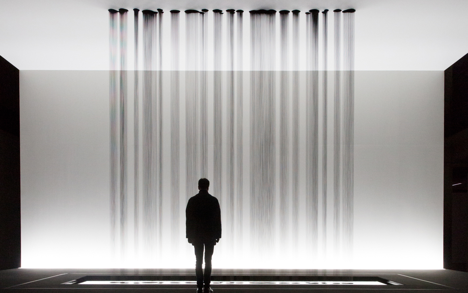 A person stands in front of a sculpture, at the drop several rivulets of oil on the floor