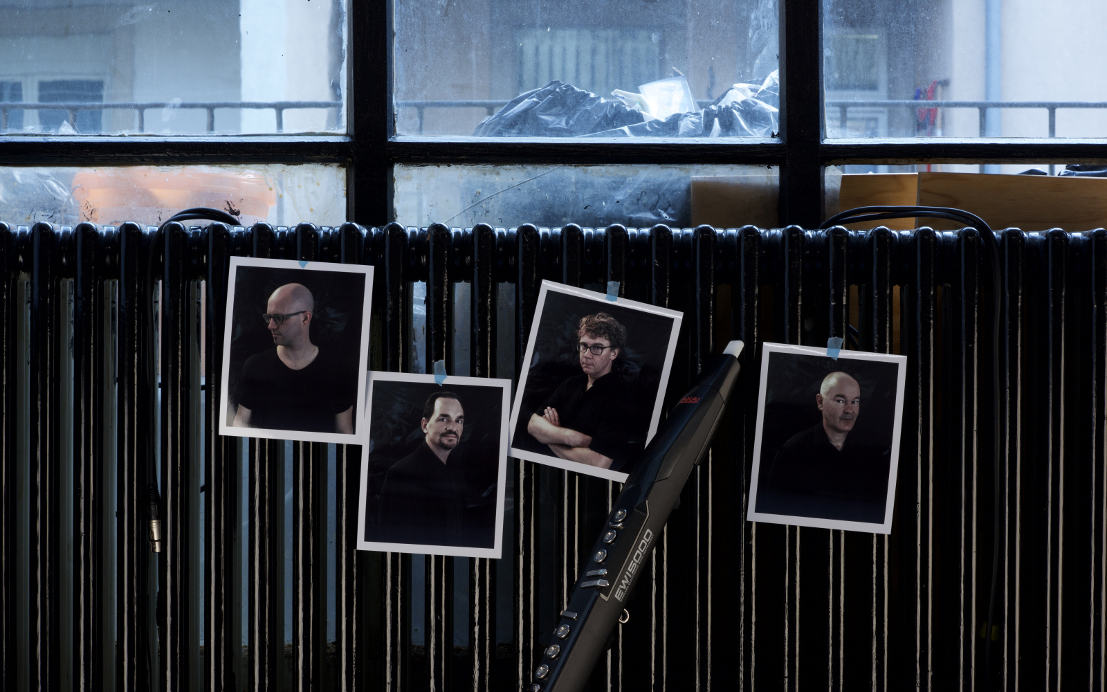 Vier Bilder von vier Männern kleben an einer Heizung. Dazwischen lehnt eine Klarinette.