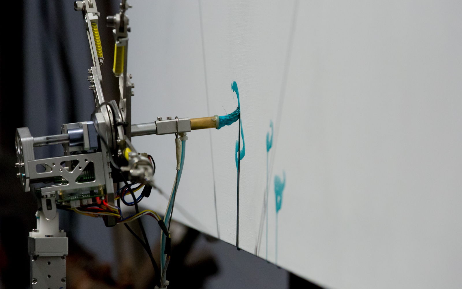  The picture shows a robot-controlled brush, drawing turquoise color on a white canvas.