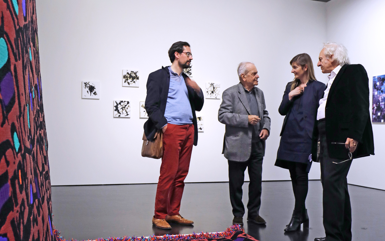 Four people are standing in front of an artwork which is a red carpet wih letters on it.