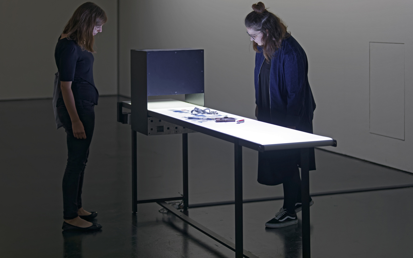  Visitors in front of a brightly lit assembly line with small objects.