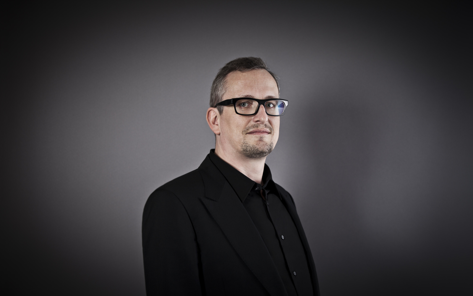Portrait von Helmut Kinzler im schwarzen Hemd vor einem dunklen einfarbigen Hintergrund