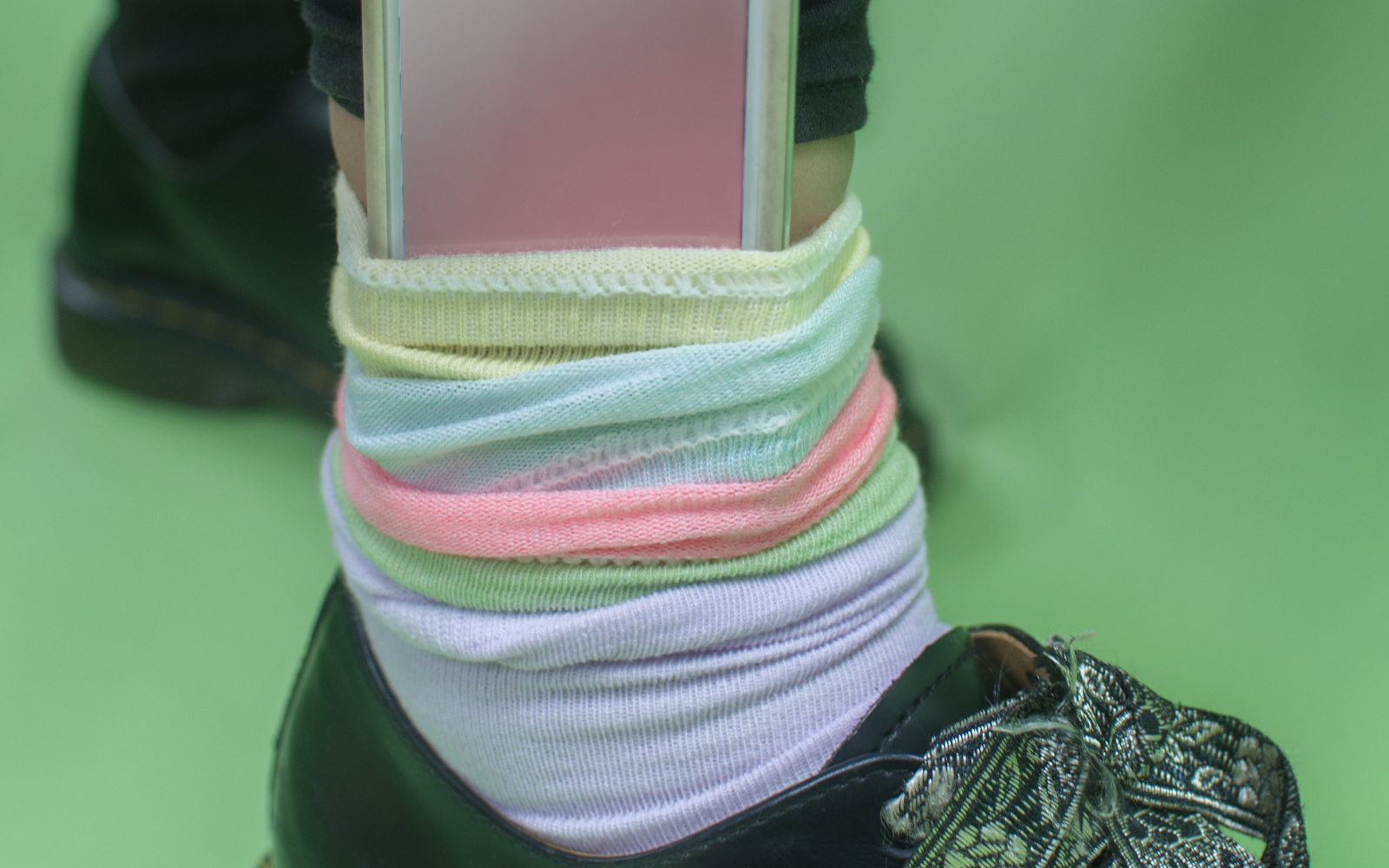 Foot and ankle with patent leather shoe and colourful sock, where a hand takes out a smartphone