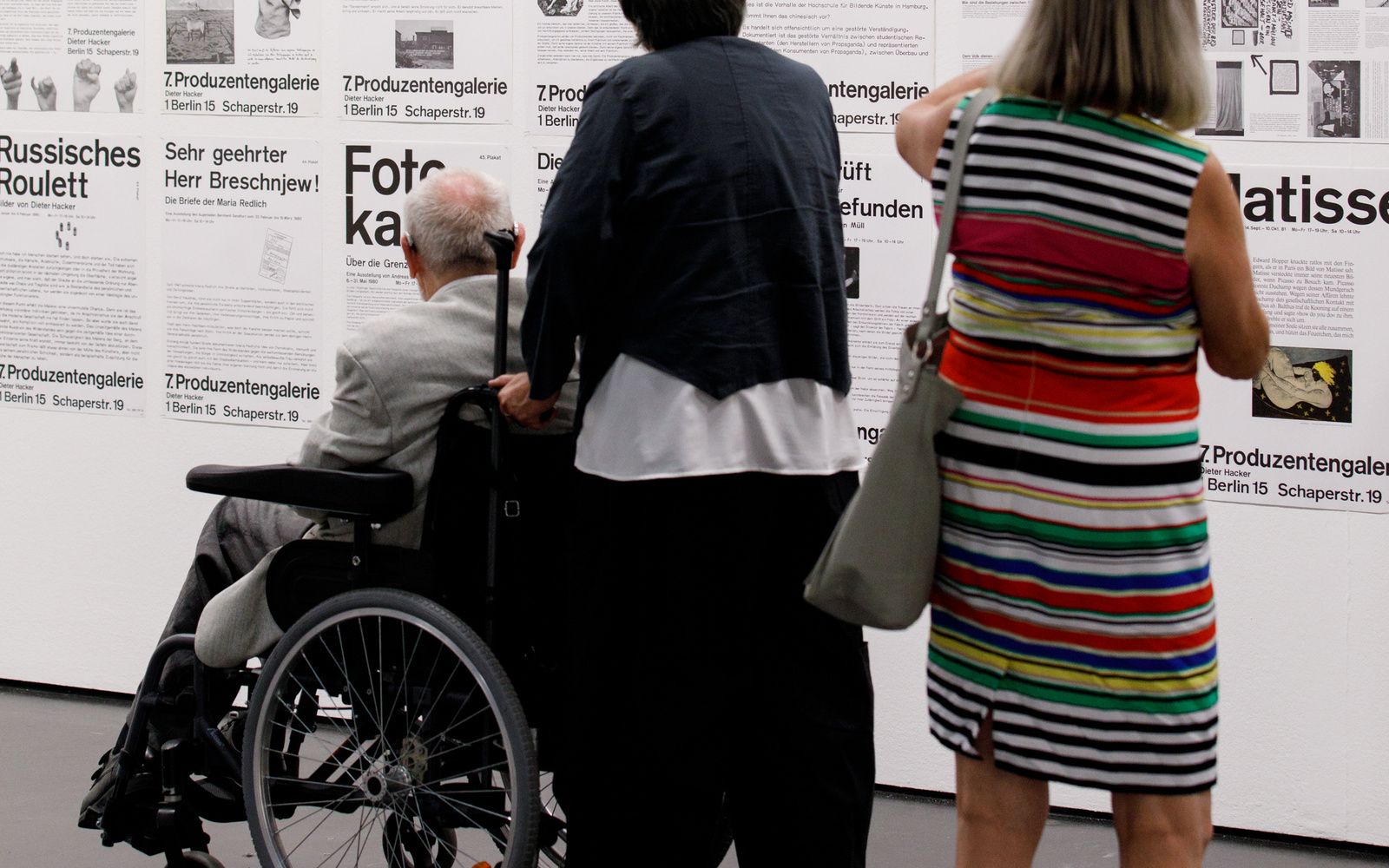 The picture shows three visitors in front of posters with typography 