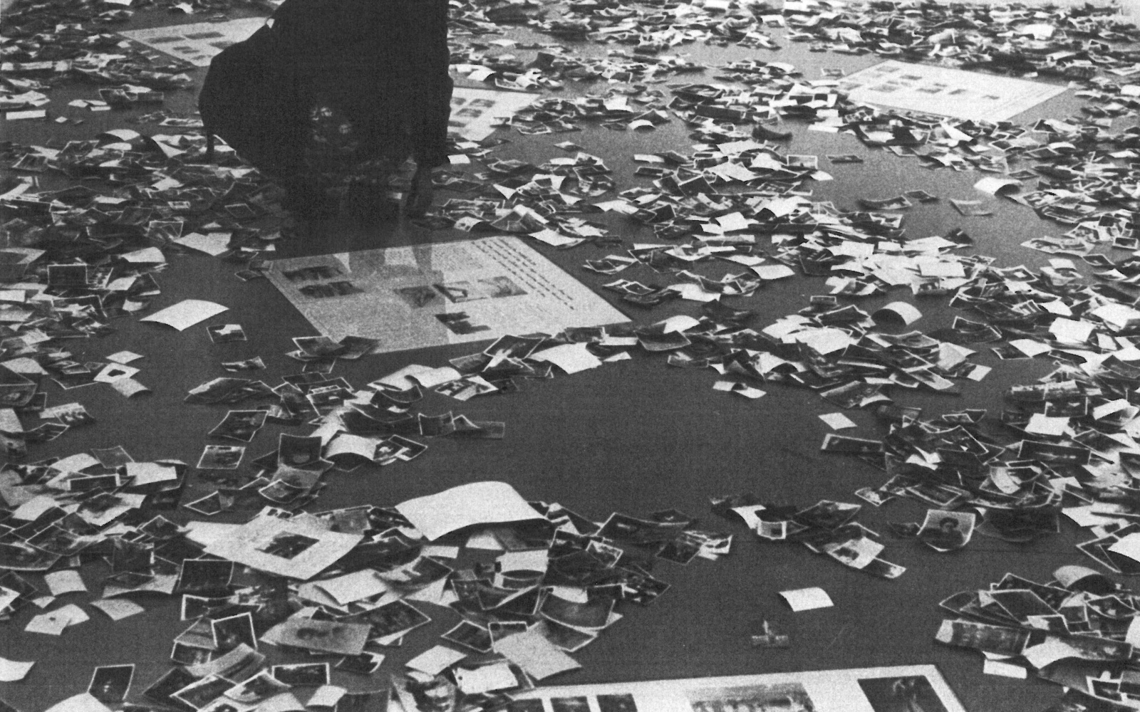 Die Schwarzweiß-Fotografie zeigt viele auf dem Boden zerstreute Fotos.