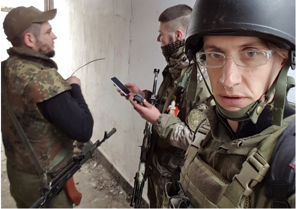 Drei Personen in Militärkleidung mit Waffen und Mobiltelefonen 