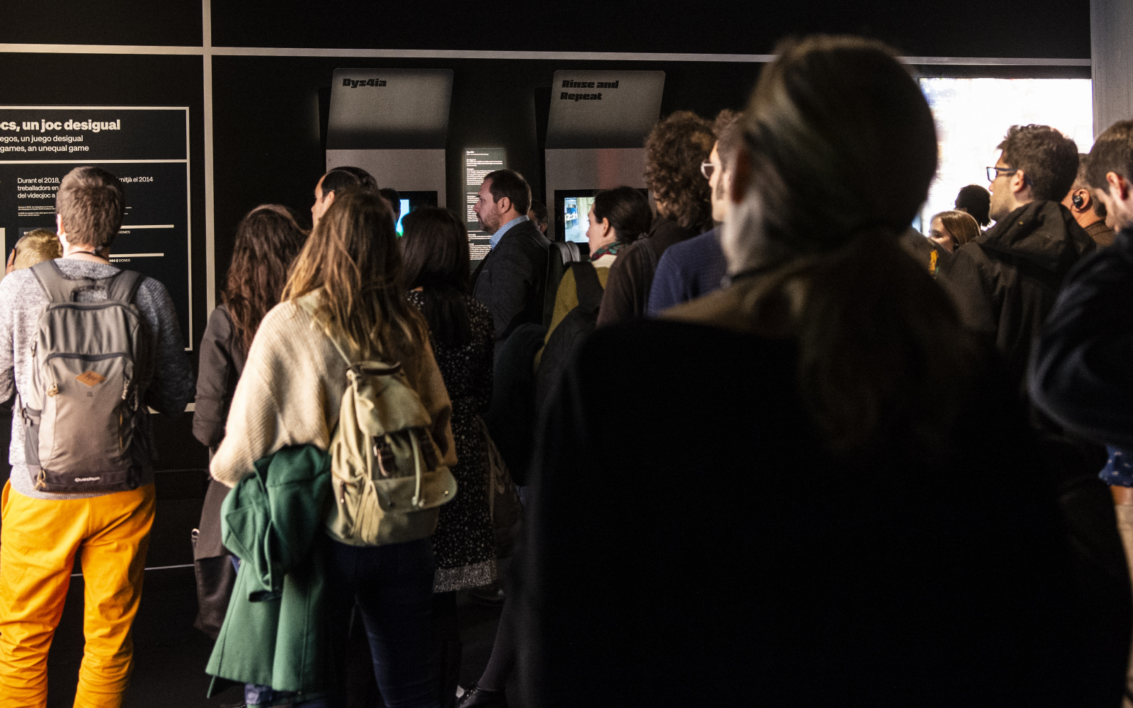 A group of people has gathered for a guided tour. You see a man on the far left with light yellow trousers, behind him is a woman with a dark green jacket hanging over her bag. They are listening attentively to the guide.