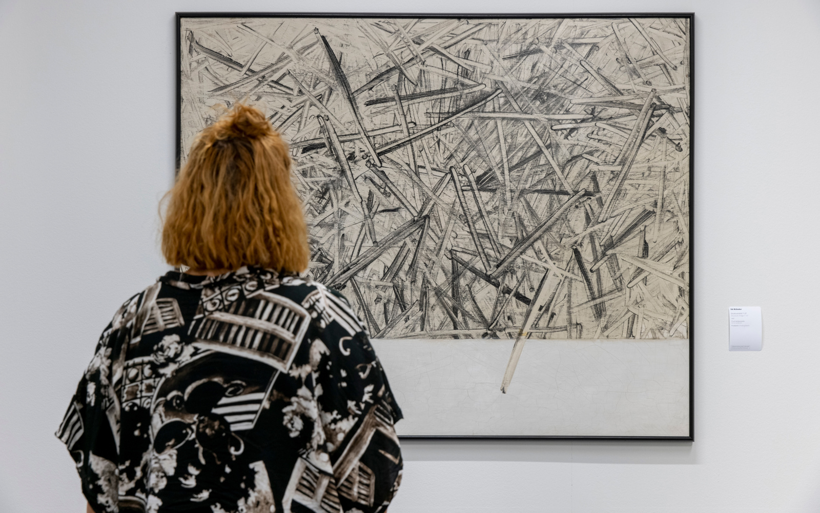 A woman is looking at a picture hung on the wall with sharp thick strokes chaotically painted on top of each other.