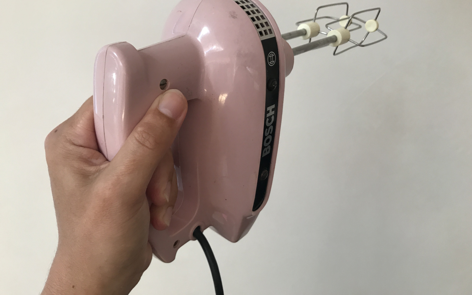 Vor einer weißen Wand wird ein rosafarbener Handrührer waagrecht hochgehoben.