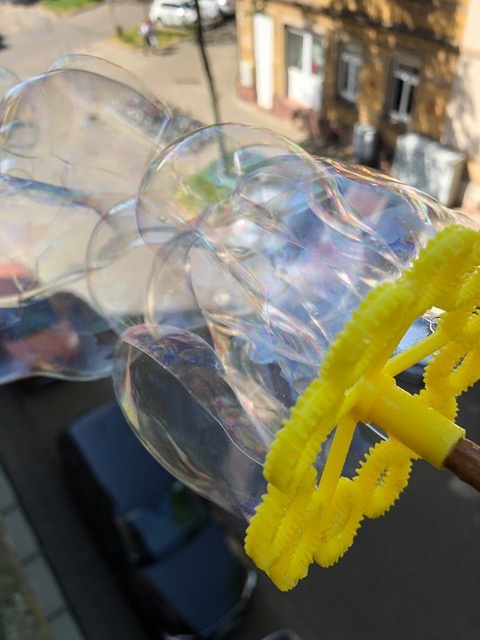 Durch ein gelbes Seifenblasenrad bläst der Wind viele schimmernden Seifenblasen.