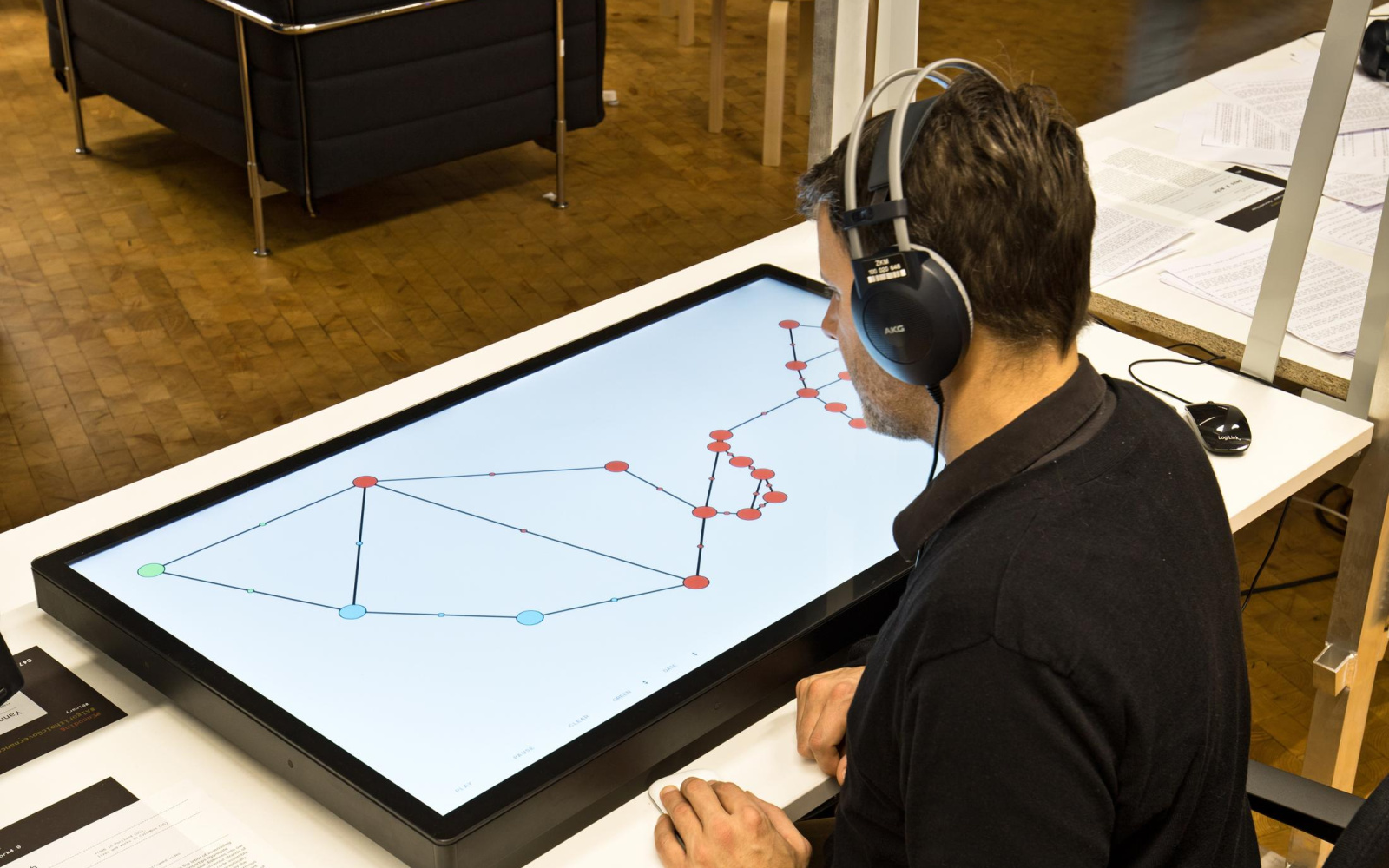 A man has headphones on and sits in front of a large screen lying on the table, which shows a graphic structure