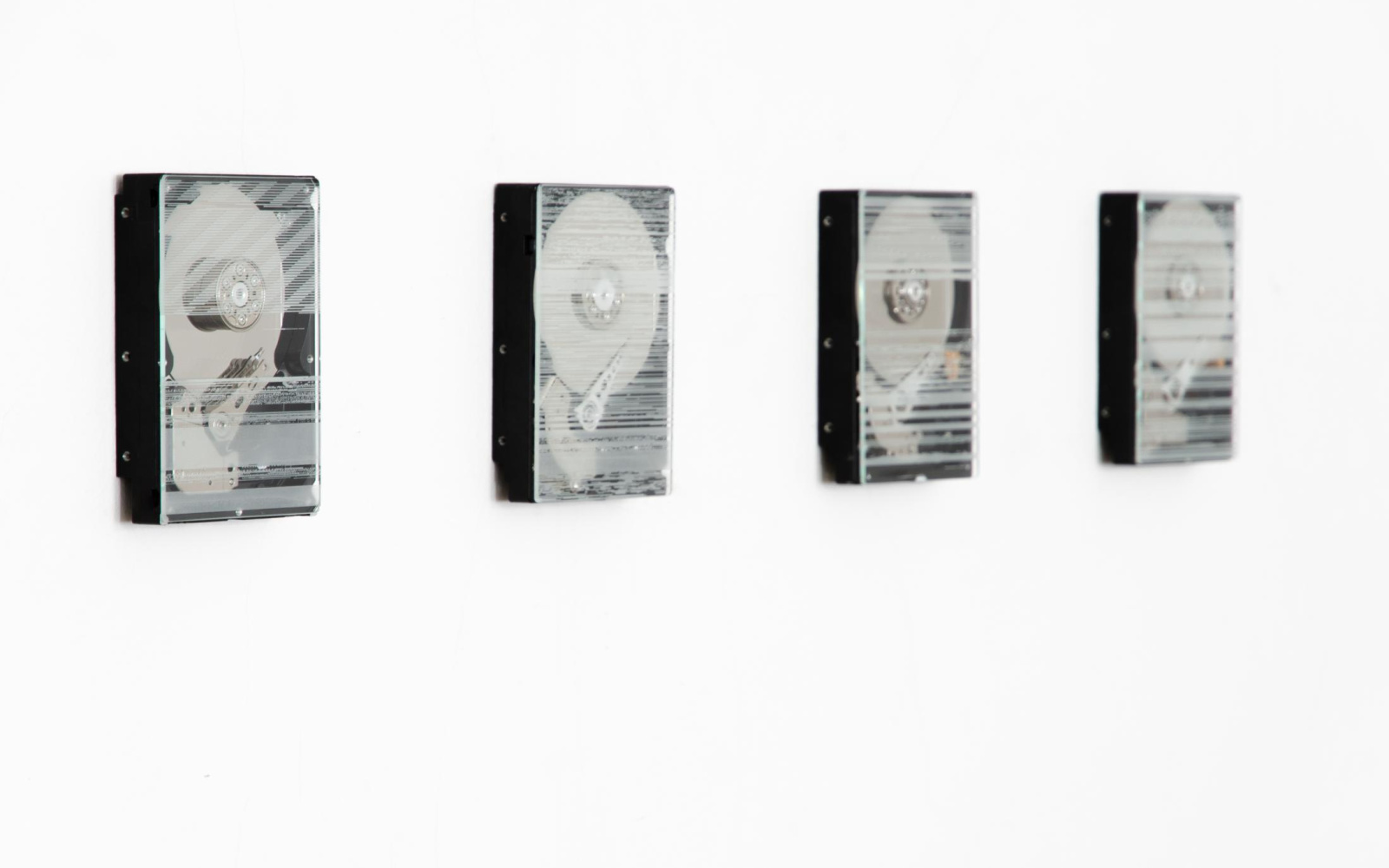 Four hard drives hang in a row on the wall. They are covered with a glass with engravings