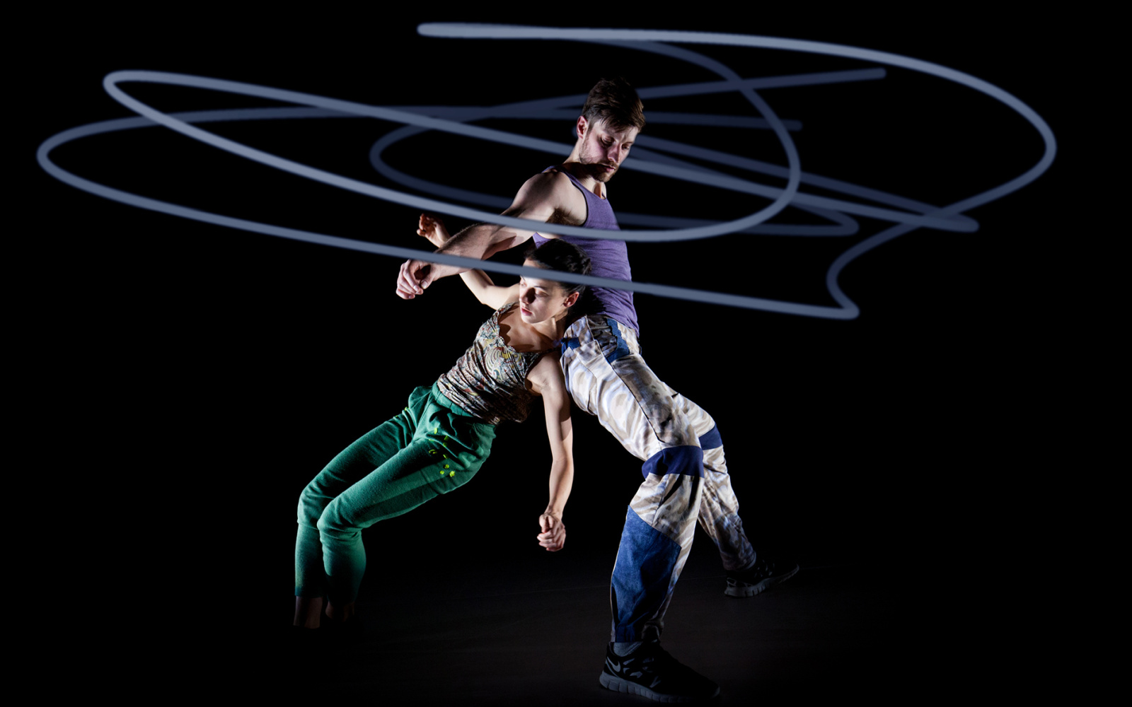 Zwei Tänzer vor schwarzem Hintergrund, umhüllt von kreisrunden Lichtkunststrahlen