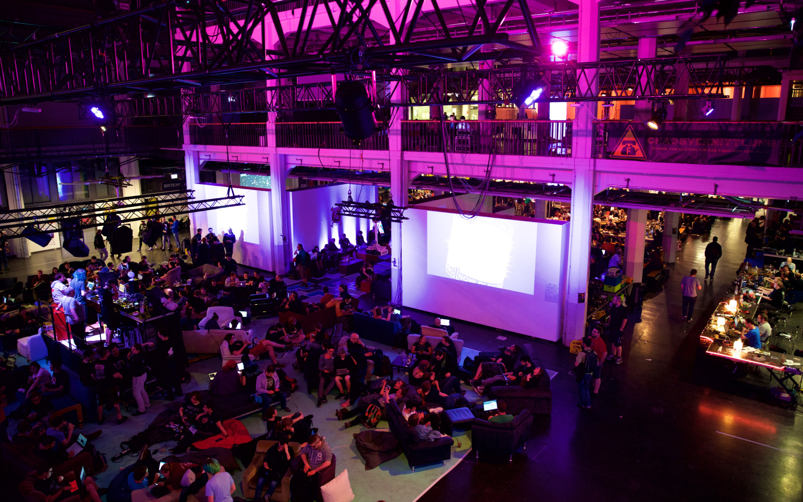 A large hall is filled with people and illuminated in pink